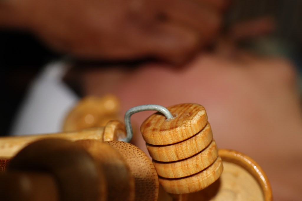 Close-up van een houten massagetool met schijven, terwijl een hand op de achtergrond een gezicht aanraakt.