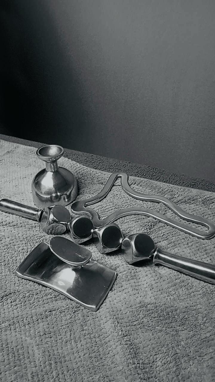 Een verzameling metalen keukengerei op een handdoek, waaronder een kan, een deegroller, en maatlepels.